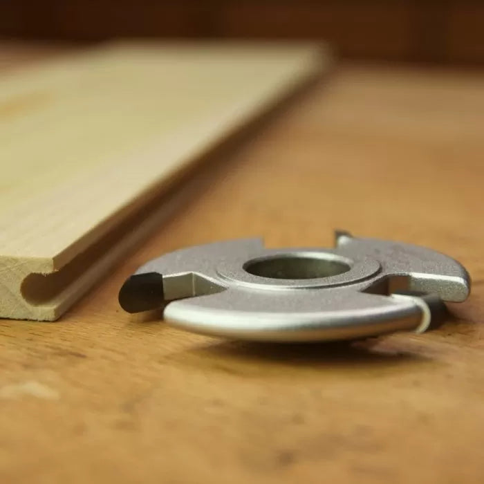 Groove cutting woodworking cutter head next to profiled wood on workbench