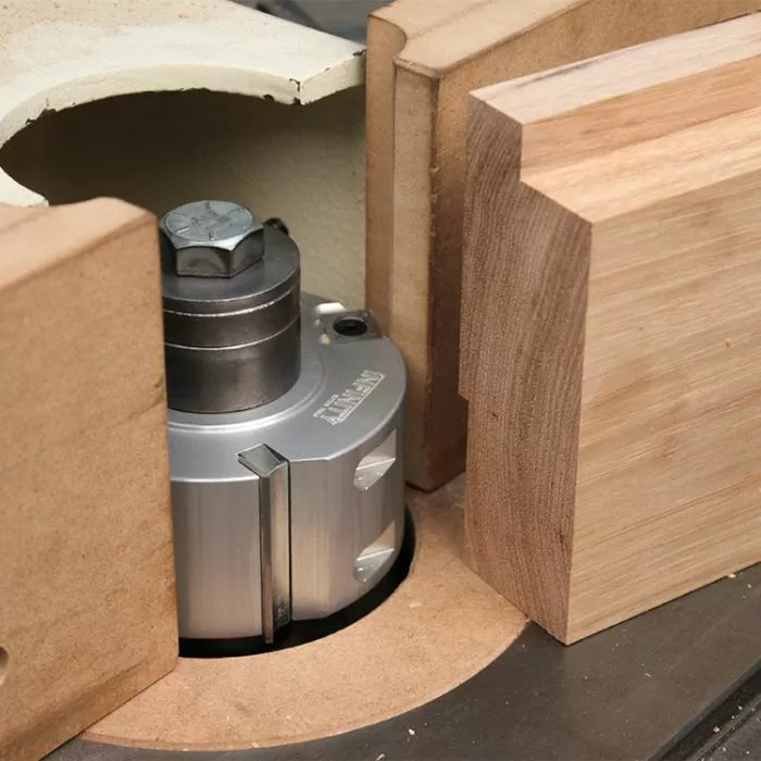 Heavy-duty woodworking shaper cutter installed on a table, surrounded by wood pieces