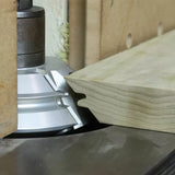 Woodworking shaper cutter head shaping a profile on a wooden board in workshop