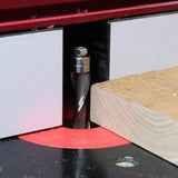 Spiral router bit cutting wood on a router table with red insert ring and fence.
