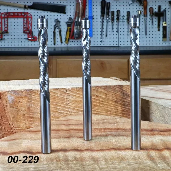 Three spiral upcut router bits for woodworking on a workshop bench with tools in background