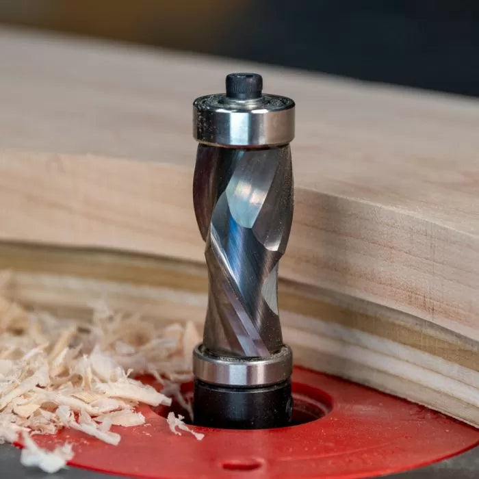 Spiral flush trim router bit cutting wood on a router table with wood shavings nearby