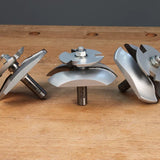 Three woodworking router bits with curved blades on wooden workbench