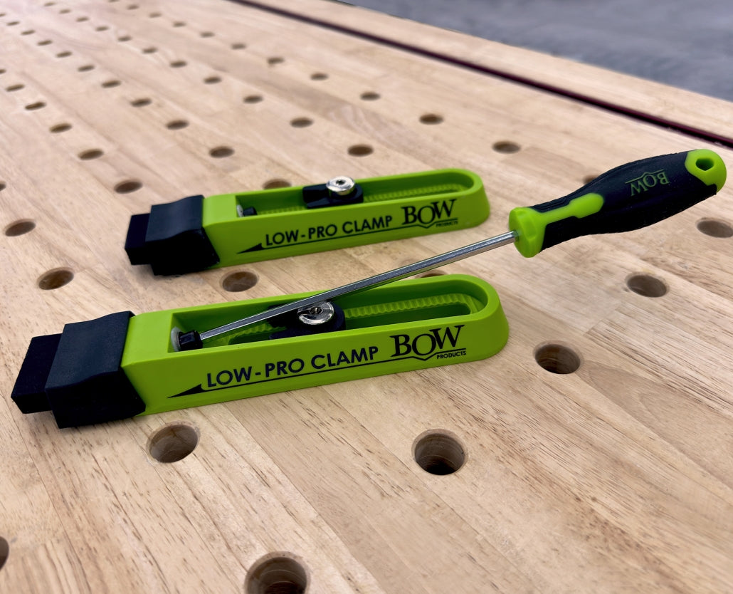 Low-profile woodworking clamps on perforated workbench, green and black color.