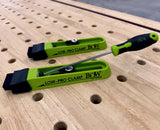 Low-profile woodworking clamps on perforated workbench, green and black color.