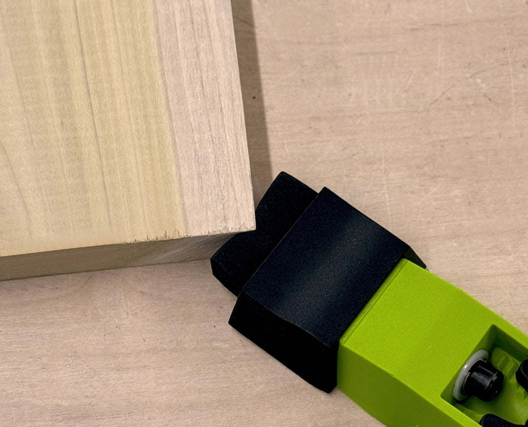Green bow clamp holding wooden board on a workbench for woodworking projects