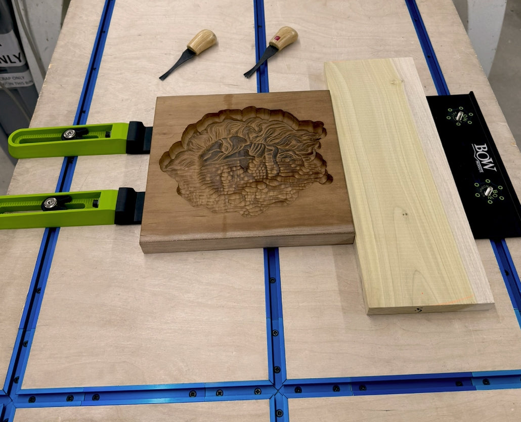 Bow clamps securing carved wooden panel and board on woodworking workbench with chisels