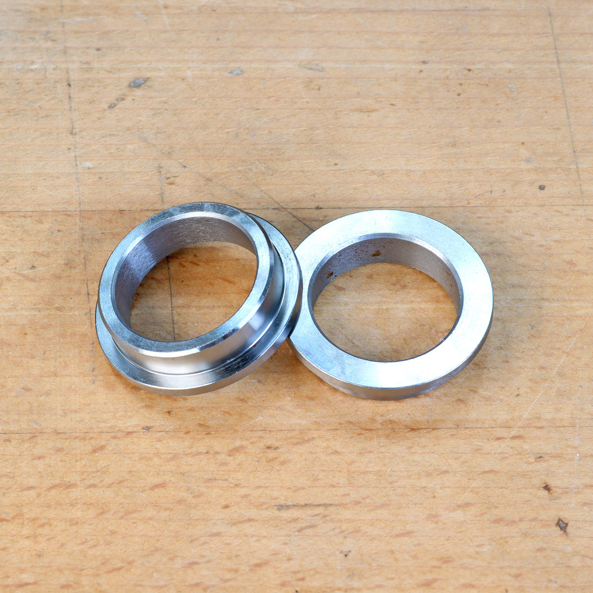 Two metal router table insert bushings on a wooden workbench for woodworking tools