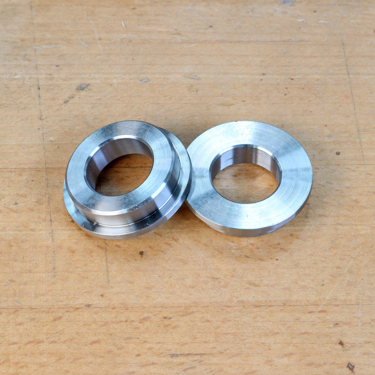 Pair of metal router table bushings on a wooden surface, woodworking tool accessories