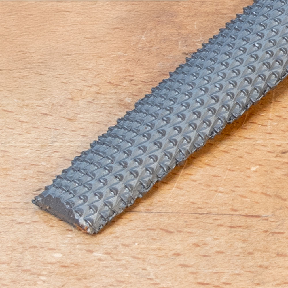 Close-up of a woodworking chisel rasp with textured steel blade on a wooden surface