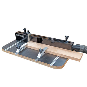 Router table fence with hold-down clamps and dust collection port holding a wood board