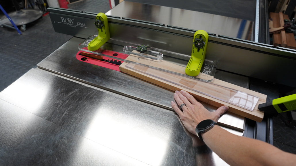 Table saw with fence and safety guides cutting wooden board in woodworking shop