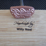 Custom wood branding iron marking 'Handmade by Willy Noel' on a wooden surface