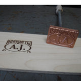 Custom branding iron for woodworking with 'Handcrafted by A.J.' stamp on wood surface.