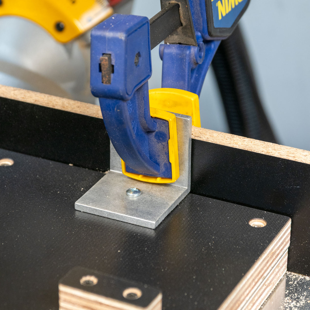 Aluminum angle miter jig bracket secured with clamp to woodworking jig base