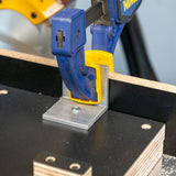 Aluminum angle miter jig bracket secured with clamp to woodworking jig base