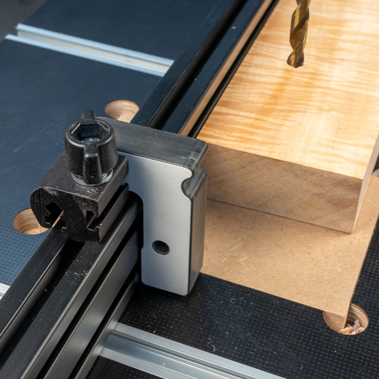 Woodworking stop block on T-track fence with wood and drill bit on workbench