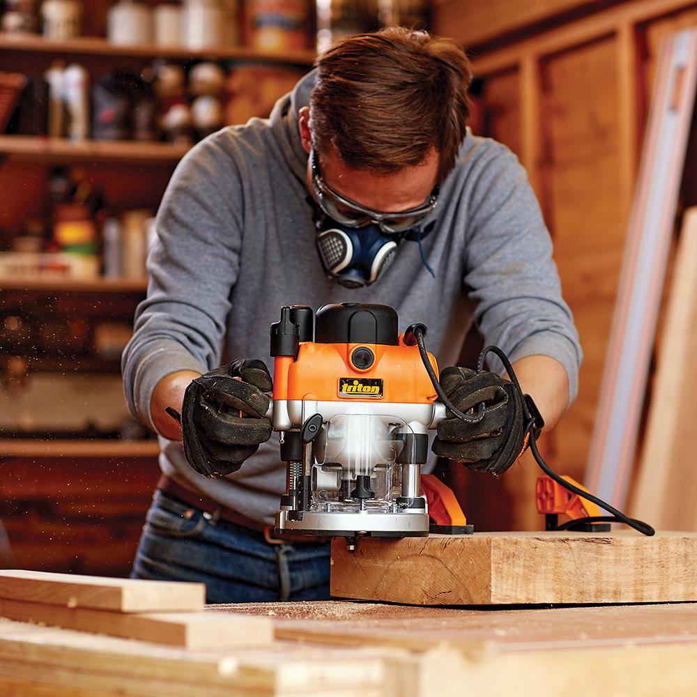 Woodworker using a plunge router on a wooden board in a workshop