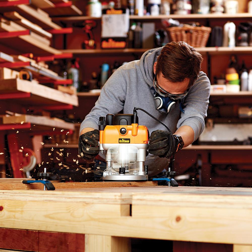Woodworker using router tool on workbench with wood chips flying in workshop setting