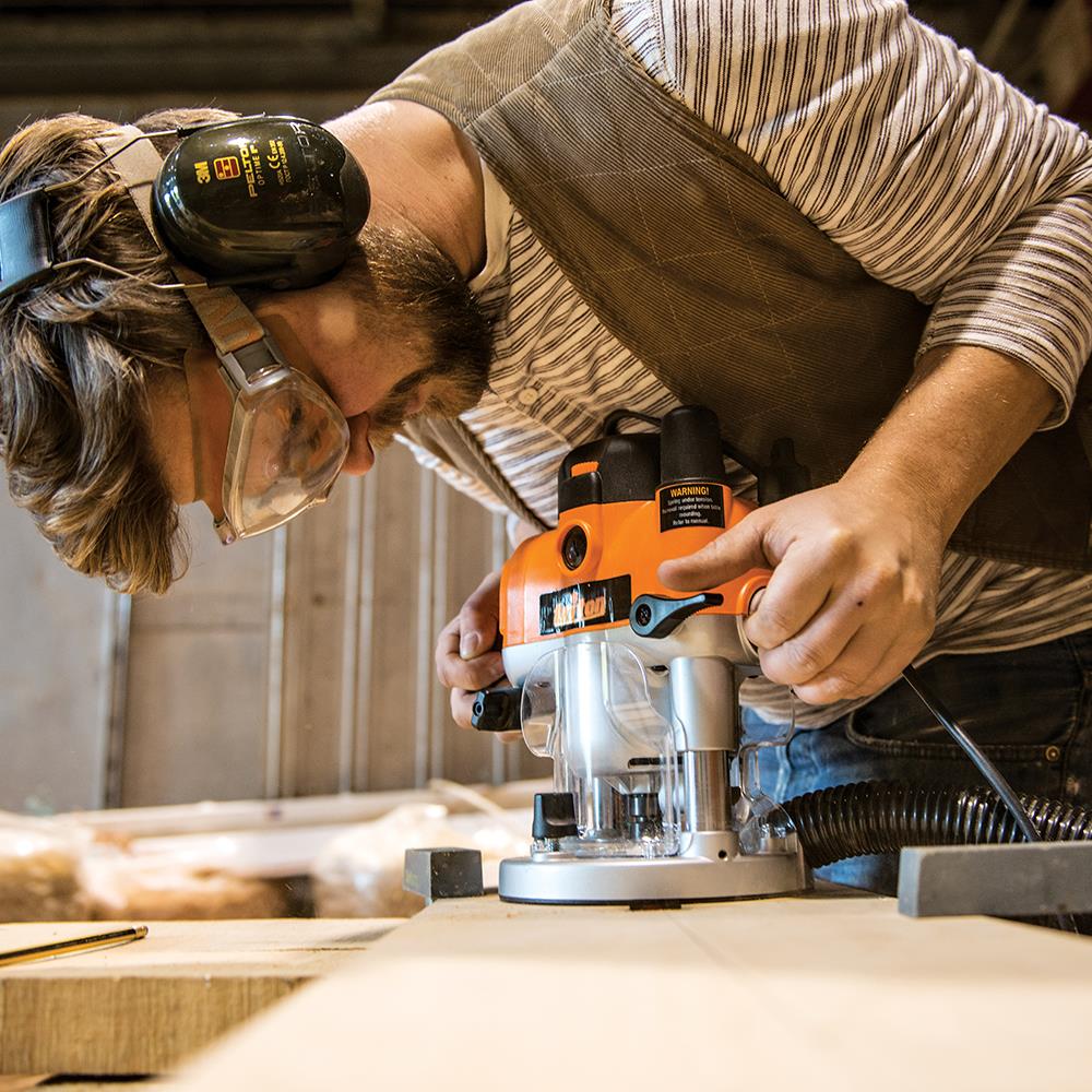 Woodworker using a plunge router tool on a wooden board in a workshop