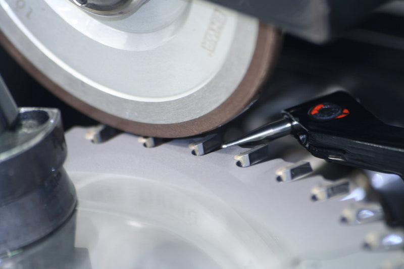 Close-up of a motorcycle chain and sprocket with a tool.