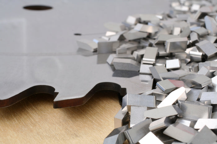 Metallic carbide saw blade tips on a wooden surface with a white background