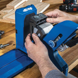 Hands adjusting a blue pocket hole jig on a wooden workbench with woodworking tools
