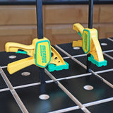 Yellow and green woodworking clamps securing material on a grid-patterned workbench