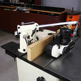 Woodworking power feeder mounted on a table saw with a fence in a workshop setting