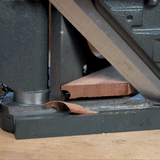 Close-up of a miter trimmer cutting a precise angle on a piece of wood, showing shavings.