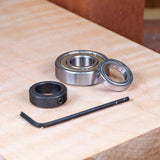 Router bearing kit with two ball bearings, a black collar, and hex key on a wooden surface
