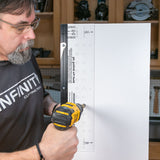 Man using a drill and shelf pin jig to make evenly spaced shelf holes on a wood panel