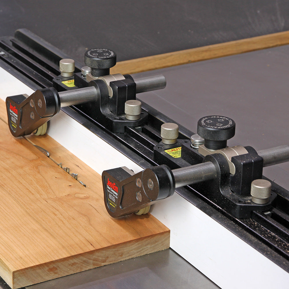 Woodworking table saw fence with dual featherboard hold-downs securing wood for precise cutting