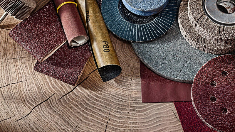Assorted sandpaper grits and sanding discs for drywall and woodworking on a wooden surface