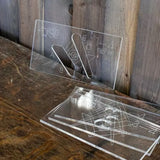 Clear acrylic router templates with etchings for woodworking, displayed on a rustic table