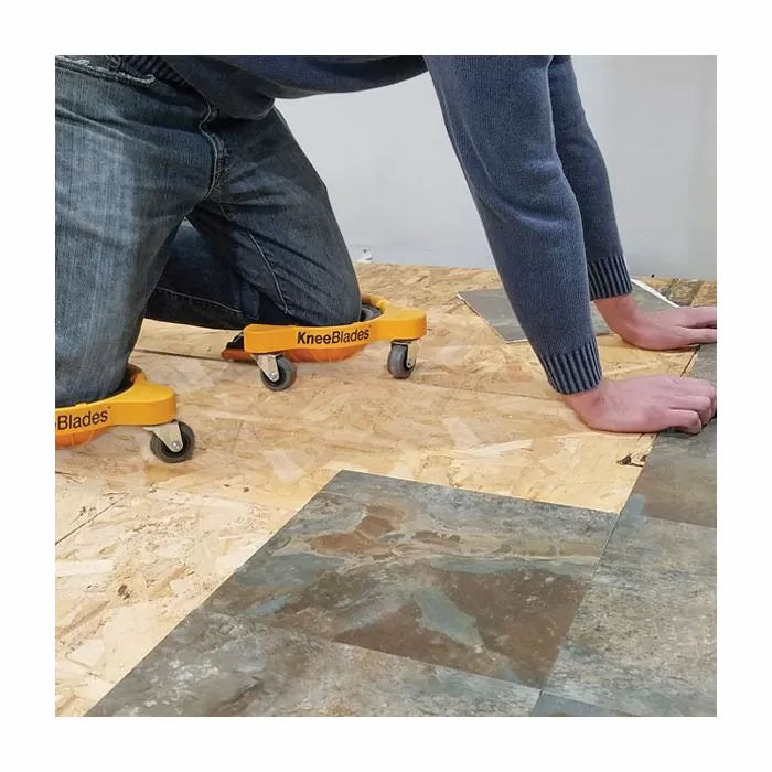 Person installing flooring with yellow KneeBlades knee pads on caster wheels