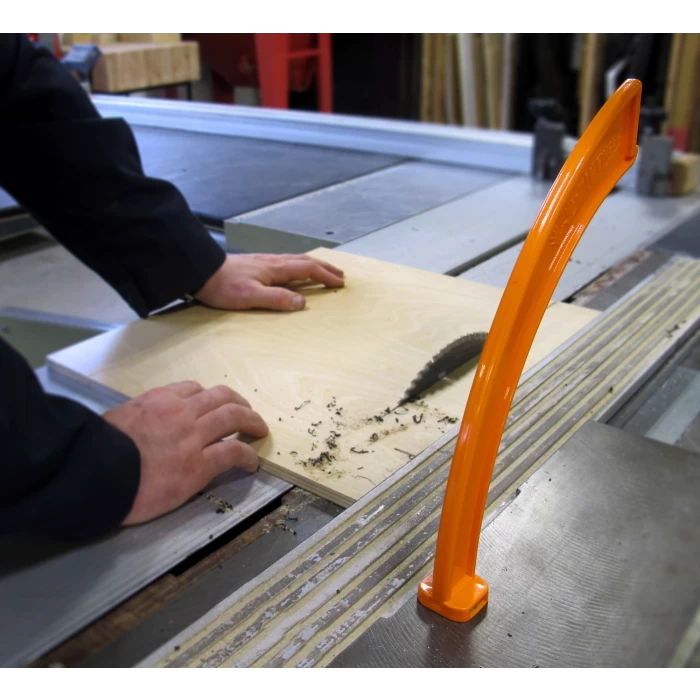 Table saw in use cutting plywood, with orange push stick for safety in woodworking shop