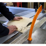 Table saw in use cutting plywood, with orange push stick for safety in woodworking shop