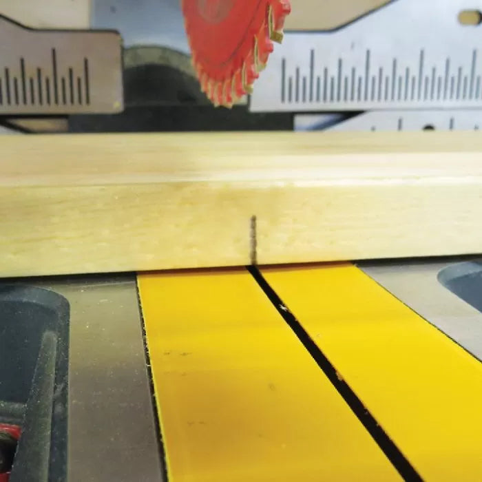 Close-up of table saw blade aligned with marked wooden board for precise woodworking cut