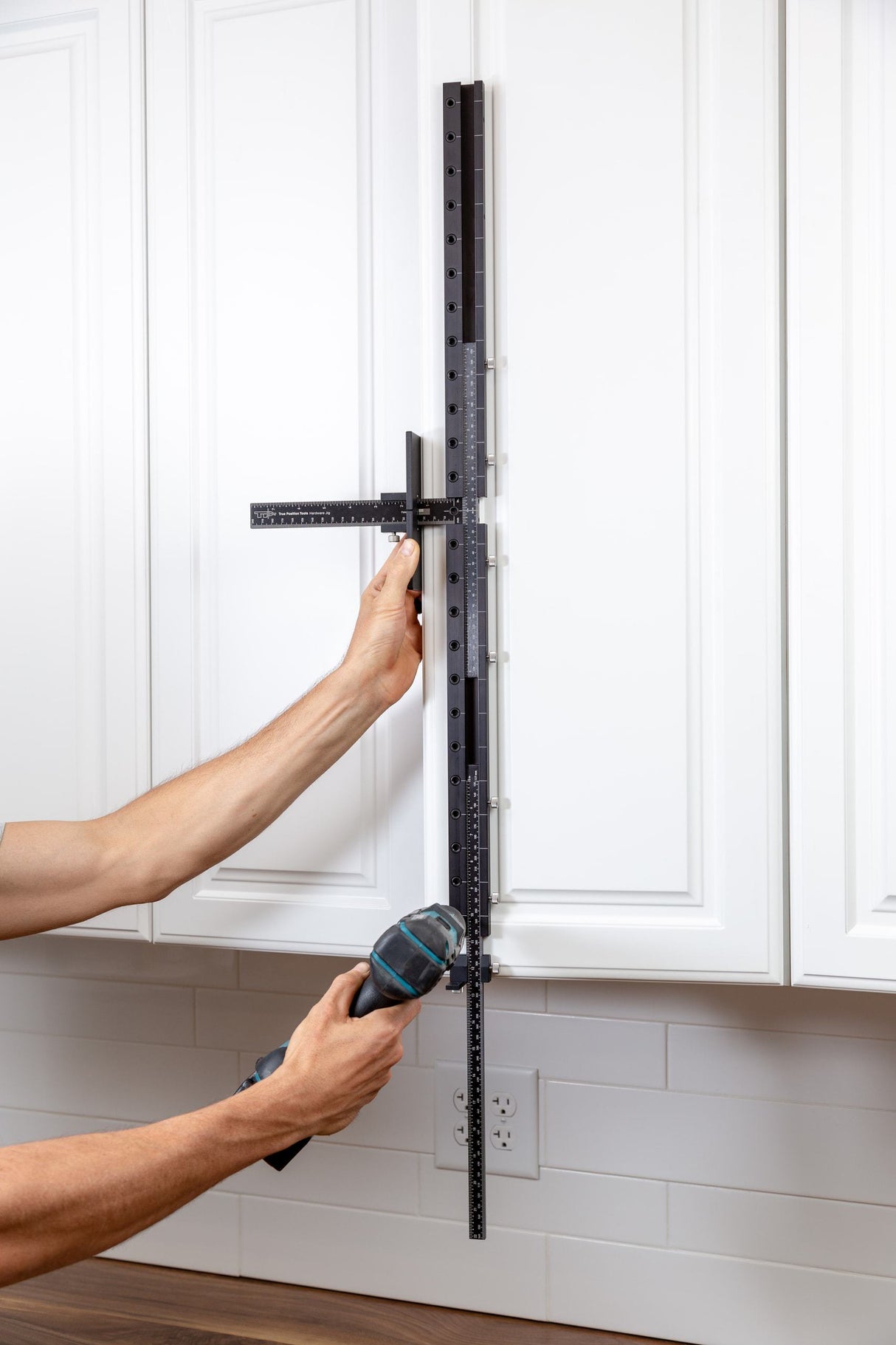 Woodworking cabinet hardware jig used to measure and drill holes on white kitchen cabinets
