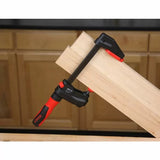 Woodworking clamp securing two wood boards on a workbench in a workshop setting