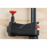 Close-up of woodworking clamp with black body and red adjustment knobs on wood surface