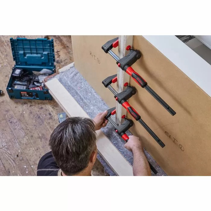 Woodworker using three bar clamps to hold boards together in a workshop setting