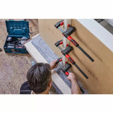 Woodworker using three bar clamps to hold boards together in a workshop setting