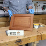 Applying wood finish to cabinet door with steel wool and Liberon wax in woodworking shop