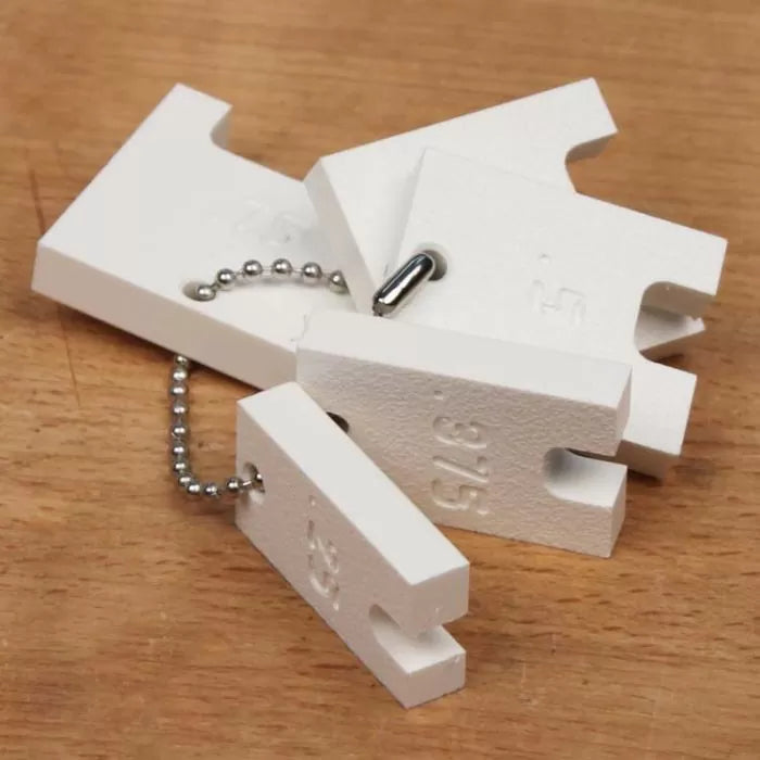 Set of white router setup blocks with measurement markings on a wooden surface