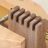 Close-up of a woodworking dovetail joint cut in dark wood, held in a wooden vise