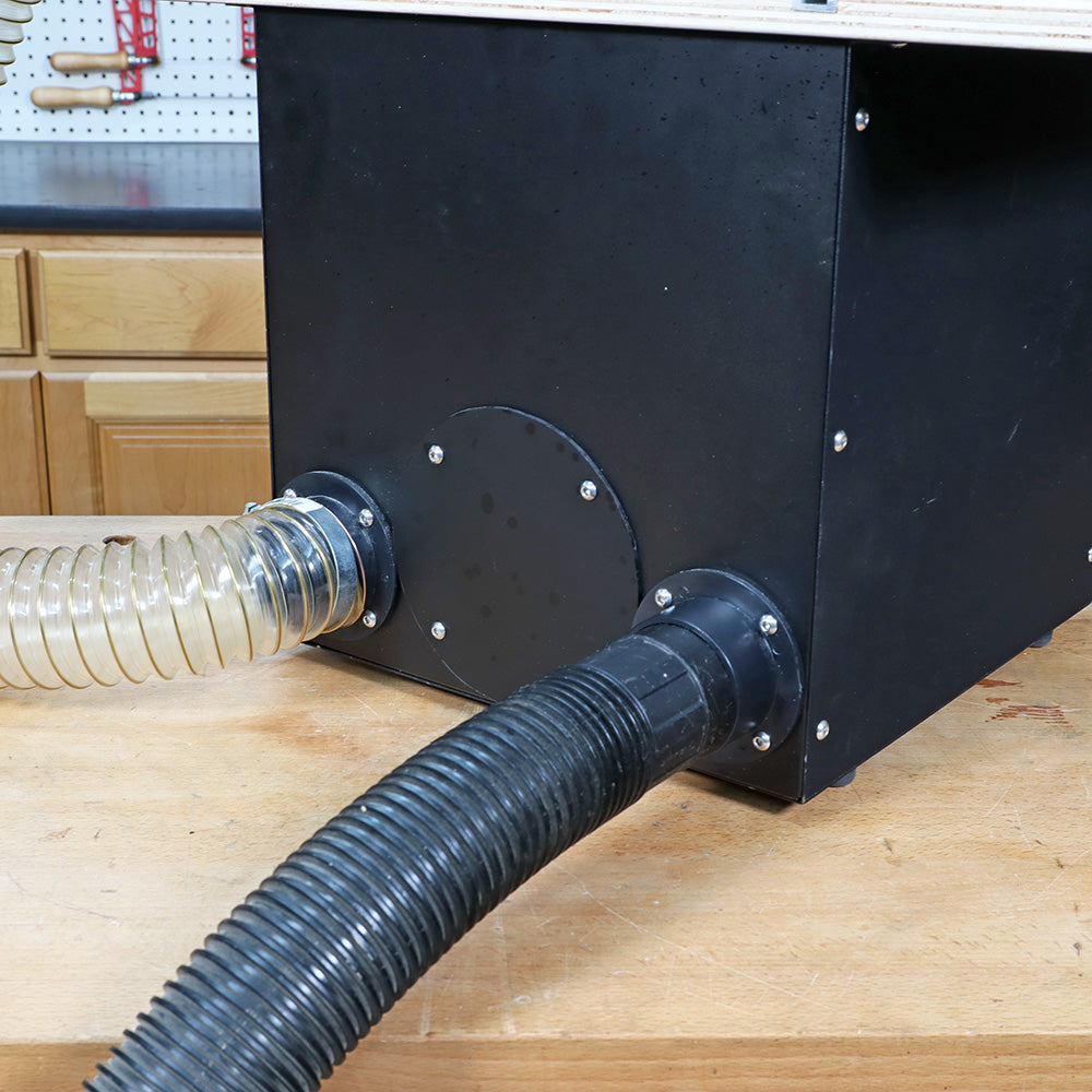 Woodworking dust collection box with attached flexible vacuum hoses on a workbench