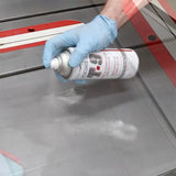 Gloved hand spraying T-9 lubricant on a table saw surface for rust prevention and tool maintenance.
