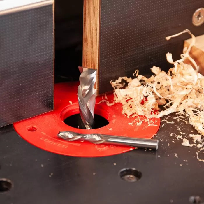 Spiral router bit cutting wood on router table with wood shavings and extra bit nearby